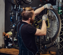 handsome redhead male jeans coverall working with bicycle wheel repair shop worker removes bicycle tire workshop
