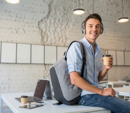 happy young handsome man sitting table headphones with backpack co working office drinking coffee